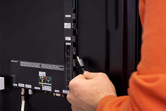 Hand mit HDMI-Kabel an den Fernseher-Anschlüssen auf der Rückseite des TV-Geräts