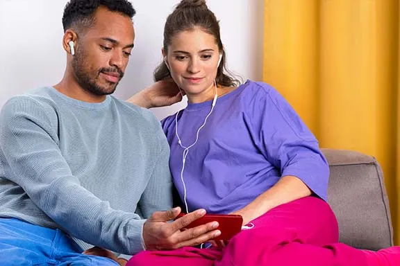 Paar schaut am Handy ein Video mit Bluetooth-Kopfhörern